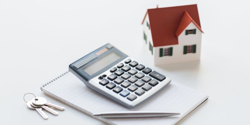 Fake Home Sitting On White Table while Calculator Sits Nearby