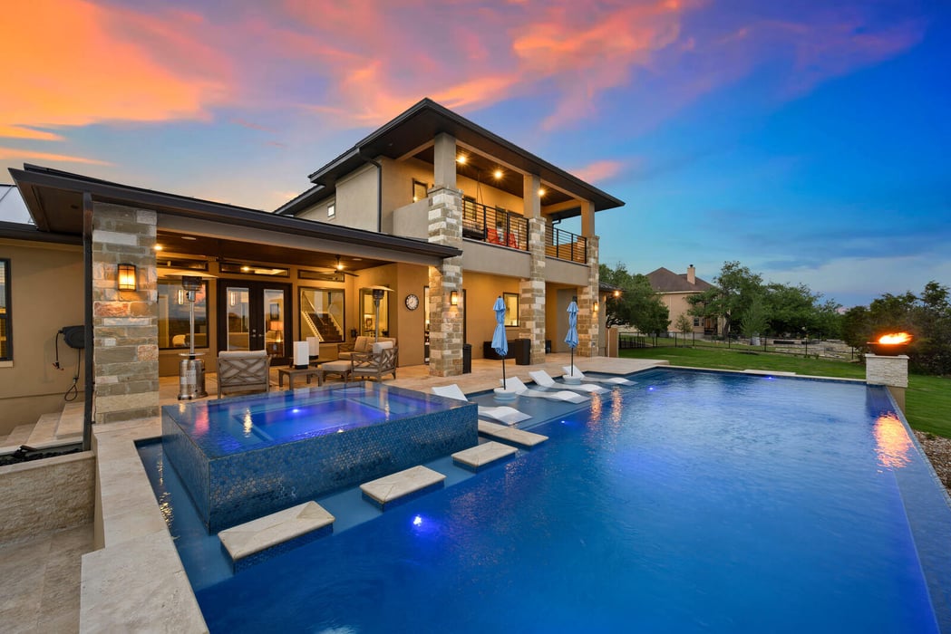 Luxury outdoor living area by Truelux Fine Homes in Austin, Texas with a pool and sunset view